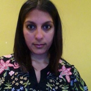 Headshot of Thrisha: brown-skinned woman with dark shoulder length hair wearing a top with flowers on. 